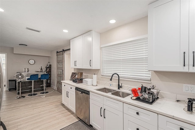 kitchen with sink, a barn door, stainless steel dishwasher, white cabinets, and light wood-type flooring