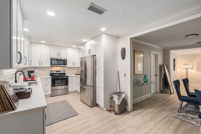 kitchen featuring white cabinetry, sink, light stone countertops, crown molding, and appliances with stainless steel finishes