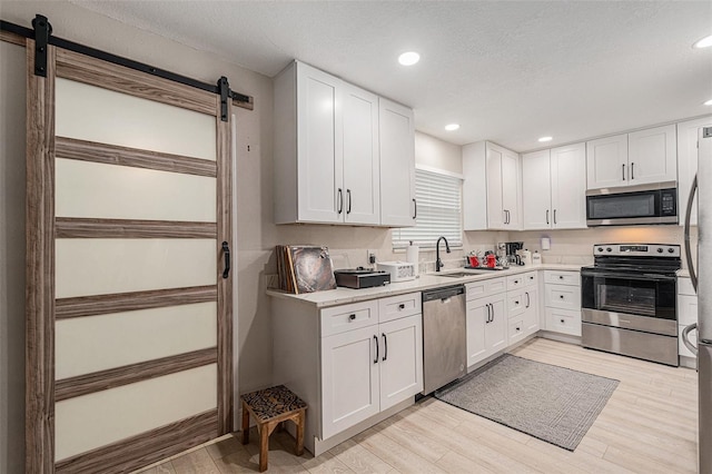 kitchen with white cabinets, appliances with stainless steel finishes, light wood-type flooring, and sink