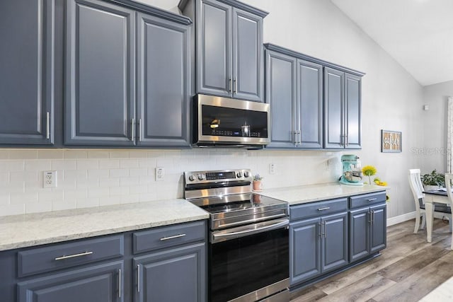 kitchen featuring backsplash, vaulted ceiling, light stone countertops, wood-type flooring, and stainless steel appliances