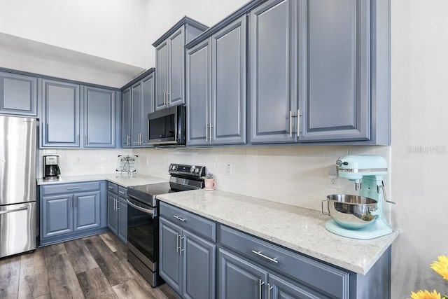 kitchen featuring dark hardwood / wood-style floors, light stone countertops, backsplash, and appliances with stainless steel finishes