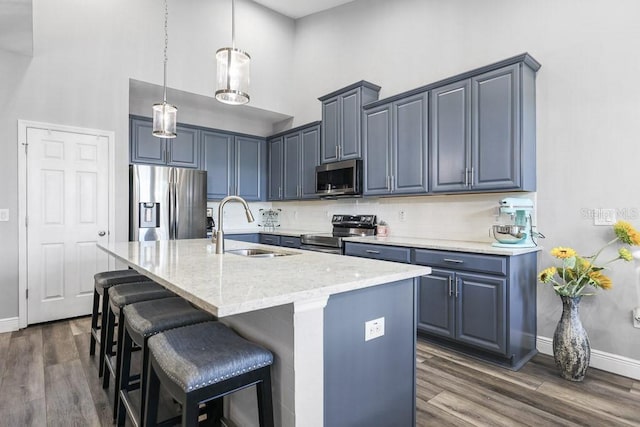 kitchen featuring dark hardwood / wood-style flooring, a towering ceiling, stainless steel appliances, a kitchen island with sink, and sink