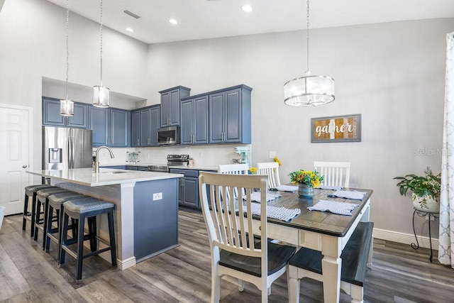 kitchen with a center island with sink, sink, decorative backsplash, a towering ceiling, and appliances with stainless steel finishes