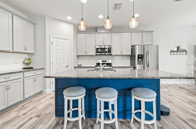 kitchen with light wood finished floors, a breakfast bar area, light stone counters, stainless steel appliances, and a sink