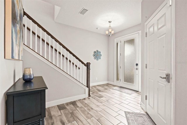 entrance foyer with light wood-type flooring, visible vents, an inviting chandelier, baseboards, and stairs