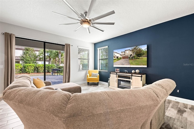 living room featuring light wood finished floors, baseboards, a fireplace, a textured ceiling, and a ceiling fan