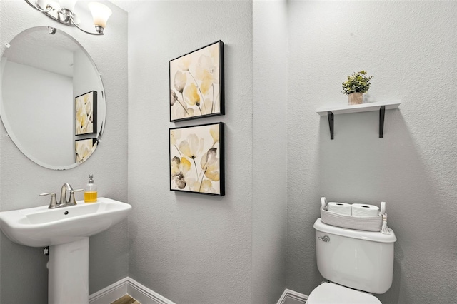 half bathroom featuring toilet, a textured wall, and baseboards