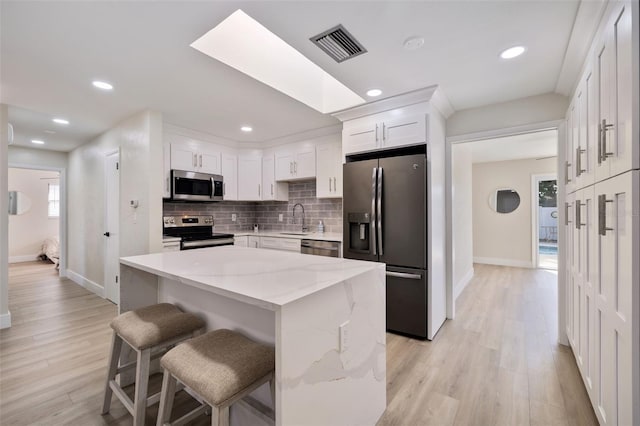 kitchen with a center island, sink, light stone counters, white cabinetry, and stainless steel appliances