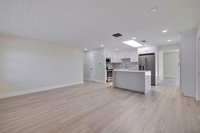 kitchen featuring a center island, backsplash, light hardwood / wood-style floors, white cabinetry, and stainless steel appliances