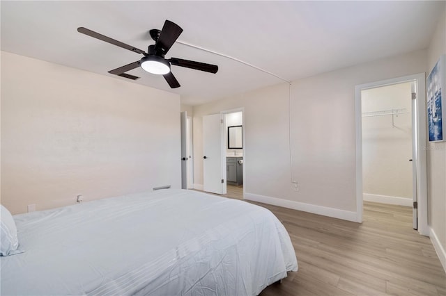 bedroom featuring ceiling fan, a spacious closet, light hardwood / wood-style flooring, ensuite bathroom, and a closet