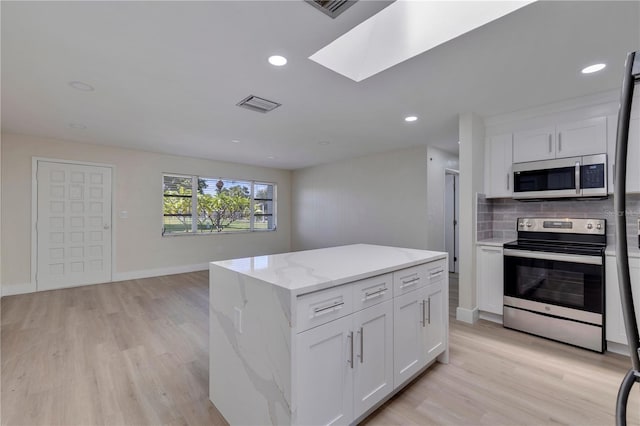 kitchen with stainless steel appliances, white cabinetry, a skylight, and a kitchen island