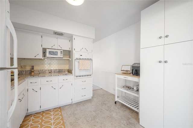 kitchen with white cabinets, light stone counters, white appliances, and tasteful backsplash