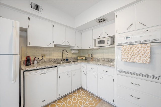 kitchen with white appliances, sink, decorative backsplash, light stone countertops, and white cabinetry