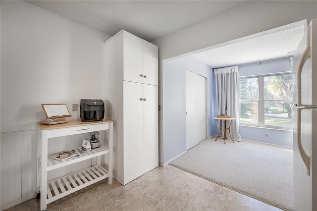 interior space featuring light carpet, a textured ceiling, white refrigerator, and white cabinets