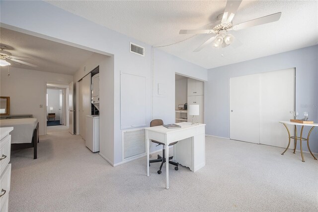 carpeted office space with a textured ceiling, ceiling fan, and stacked washer / drying machine