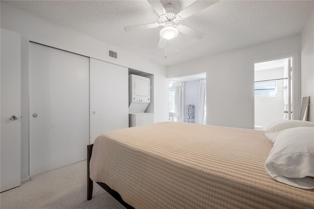 carpeted bedroom with stacked washing maching and dryer, ensuite bath, a textured ceiling, ceiling fan, and a closet