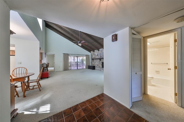 unfurnished living room featuring a stone fireplace, ceiling fan, dark carpet, and vaulted ceiling