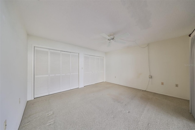 unfurnished bedroom featuring ceiling fan, light carpet, and two closets