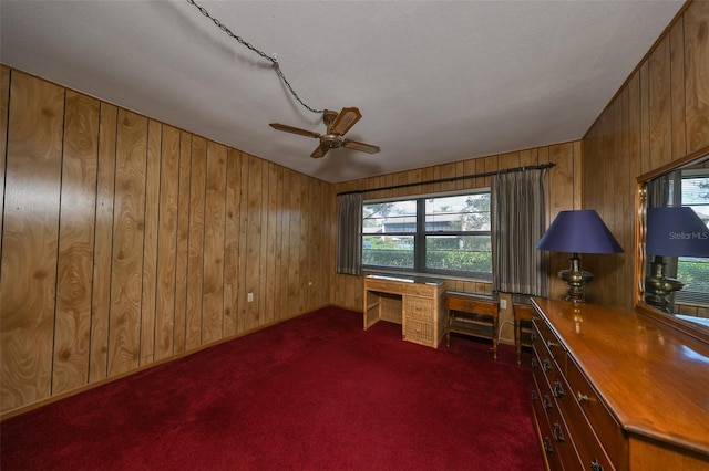 unfurnished office with wooden walls, built in desk, a textured ceiling, and dark carpet