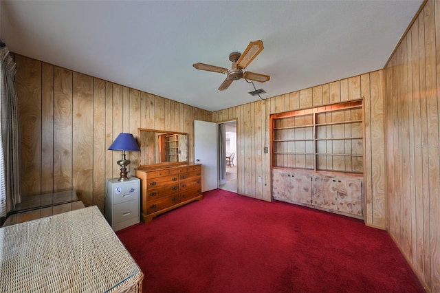 bedroom with ceiling fan, wooden walls, and dark colored carpet