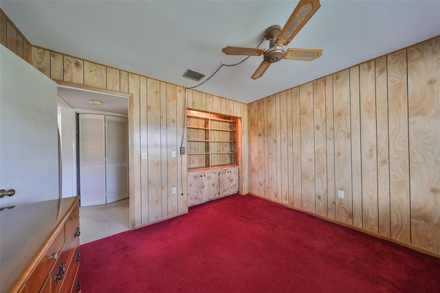 carpeted spare room featuring ceiling fan and wood walls