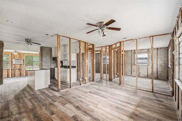 interior space featuring a wall mounted air conditioner, sink, hardwood / wood-style flooring, ceiling fan, and a textured ceiling