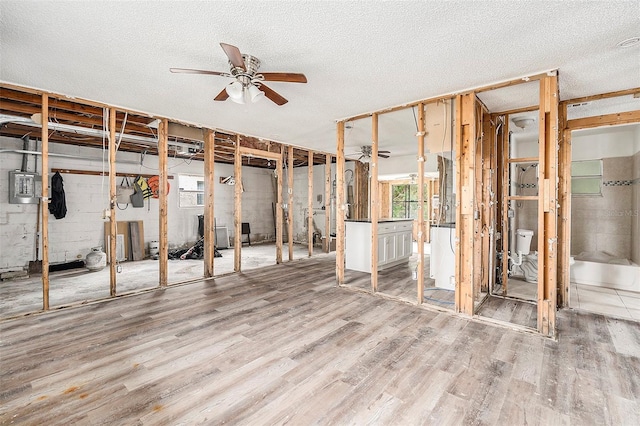 basement featuring a textured ceiling, electric panel, hardwood / wood-style flooring, and ceiling fan