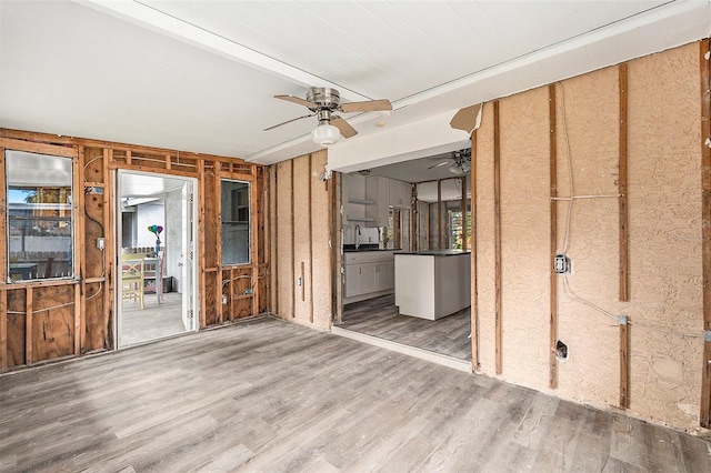 unfurnished living room featuring wooden walls, hardwood / wood-style floors, ceiling fan, and sink