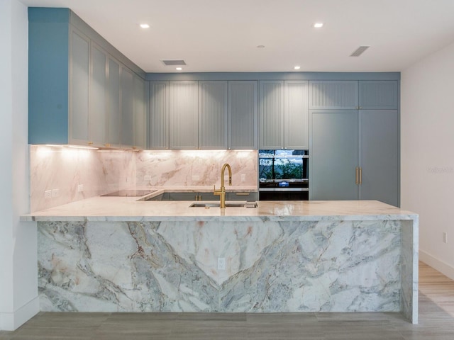 kitchen featuring sink, kitchen peninsula, light hardwood / wood-style floors, gray cabinets, and black electric stovetop