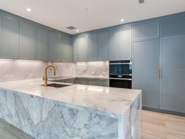 kitchen with kitchen peninsula, decorative backsplash, light stone counters, and sink