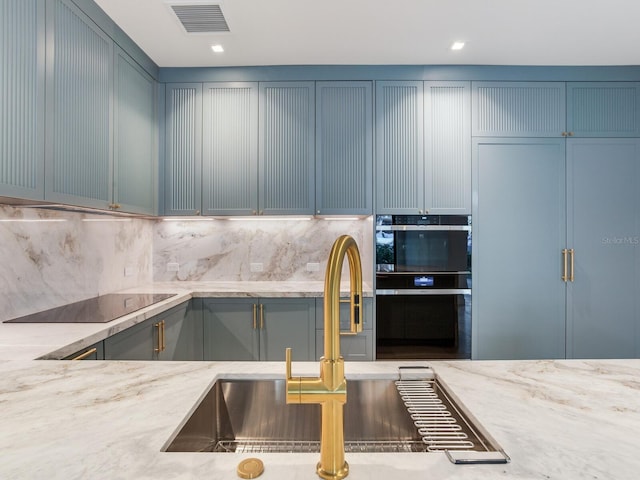 kitchen featuring backsplash, light stone counters, multiple ovens, black electric cooktop, and paneled built in fridge