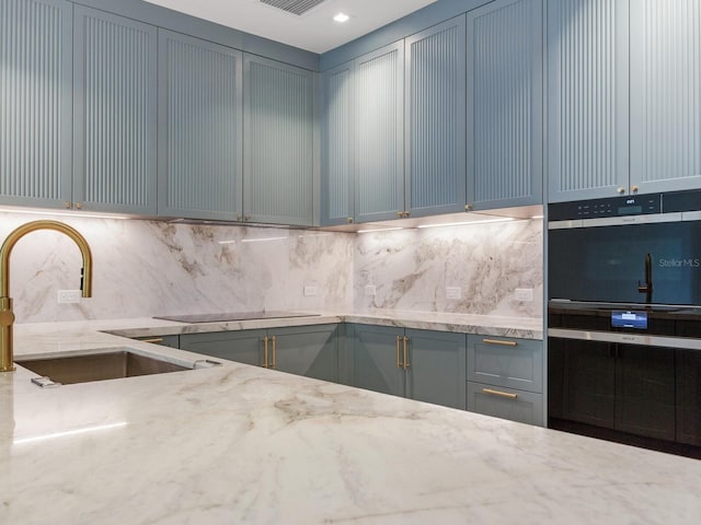 kitchen with black electric stovetop, double wall oven, tasteful backsplash, light stone counters, and sink