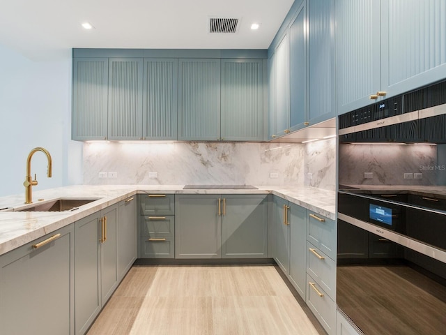 kitchen featuring decorative backsplash, black electric cooktop, light stone counters, and sink