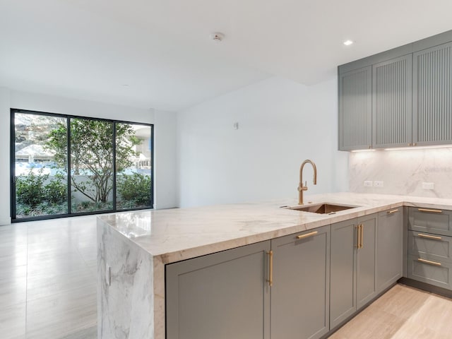 kitchen with tasteful backsplash, gray cabinetry, light stone countertops, and sink