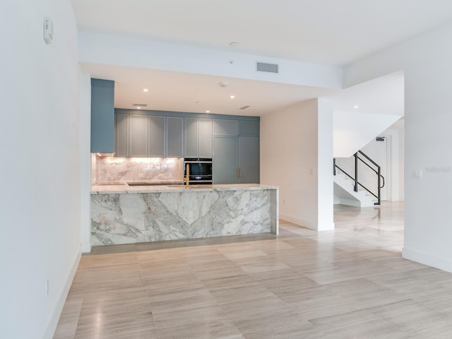 kitchen featuring light stone countertops, black double oven, tasteful backsplash, and gray cabinetry