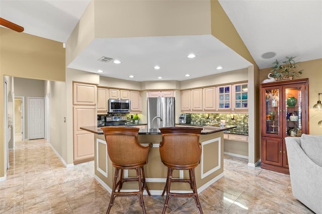 kitchen with backsplash, a breakfast bar, stainless steel appliances, a kitchen island with sink, and light brown cabinets