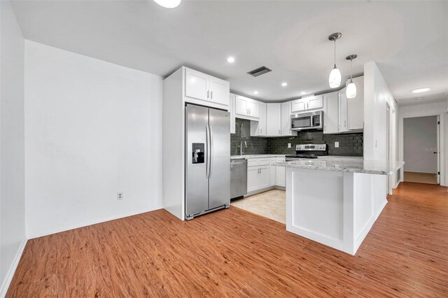 kitchen with light wood-type flooring, appliances with stainless steel finishes, white cabinets, light stone countertops, and backsplash