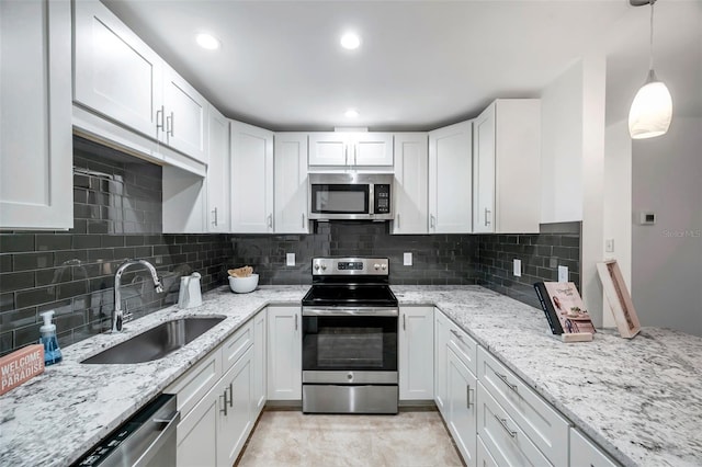 kitchen featuring sink, white cabinetry, stainless steel appliances, light stone counters, and decorative light fixtures