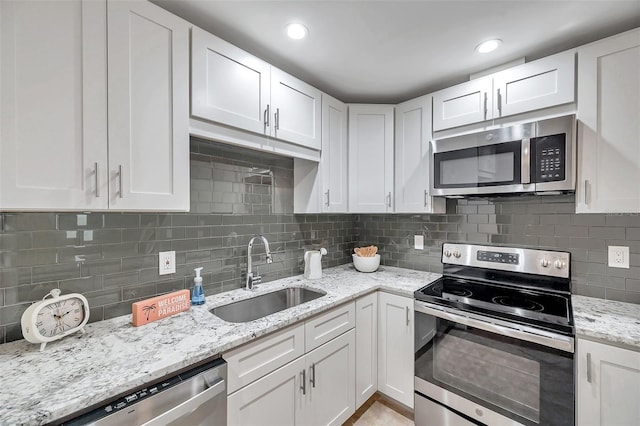 kitchen featuring sink, light stone counters, tasteful backsplash, appliances with stainless steel finishes, and white cabinets