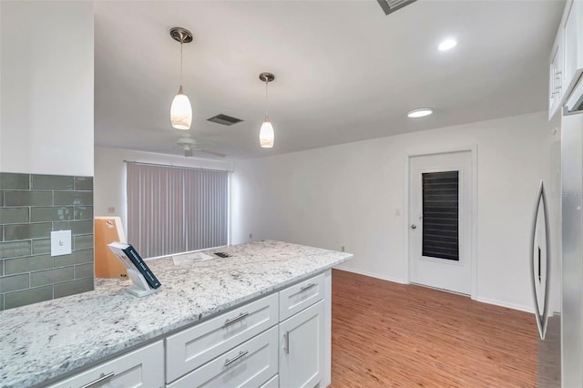 kitchen featuring white cabinetry, light wood-type flooring, pendant lighting, light stone countertops, and backsplash