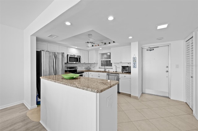 kitchen featuring tasteful backsplash, stainless steel appliances, a kitchen island, ceiling fan, and white cabinetry