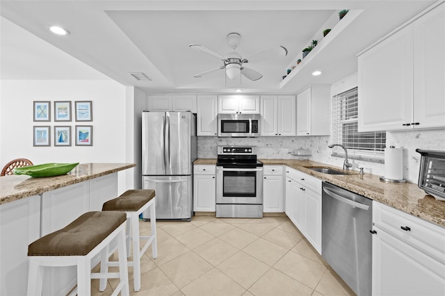 kitchen with light stone countertops, appliances with stainless steel finishes, backsplash, sink, and white cabinetry