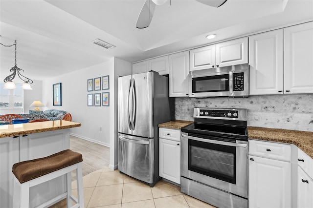 kitchen with appliances with stainless steel finishes, tasteful backsplash, light tile patterned floors, decorative light fixtures, and white cabinetry