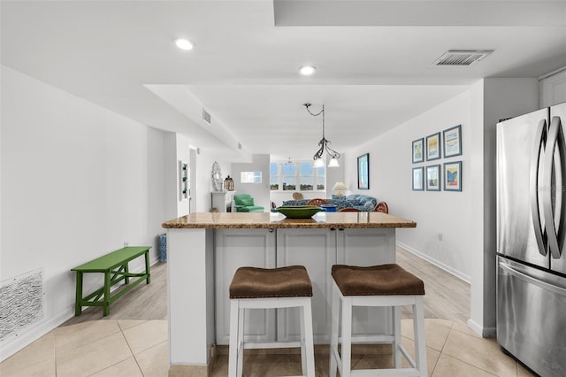 kitchen with stainless steel refrigerator, a center island, a kitchen breakfast bar, light hardwood / wood-style flooring, and pendant lighting