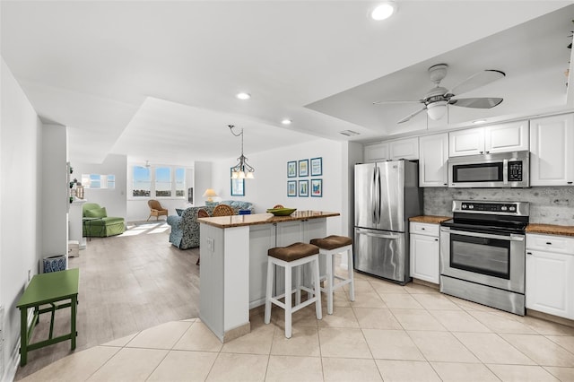 kitchen with stainless steel appliances, light hardwood / wood-style floors, decorative light fixtures, a kitchen bar, and white cabinets