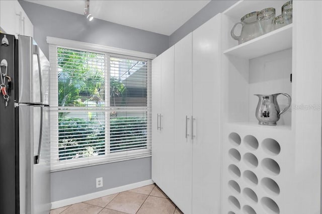 kitchen with white cabinets, light tile patterned floors, stainless steel refrigerator, and a wealth of natural light