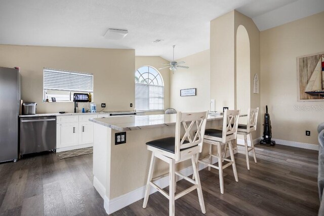 kitchen with a kitchen bar, dark hardwood / wood-style flooring, stainless steel appliances, vaulted ceiling, and white cabinets