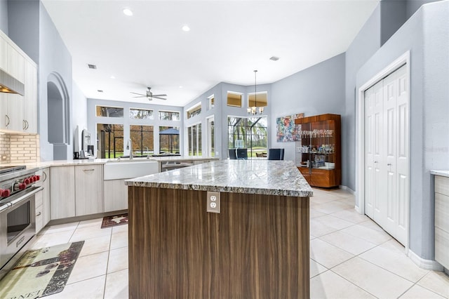 kitchen featuring light stone counters, premium range, ceiling fan with notable chandelier, sink, and light tile patterned floors