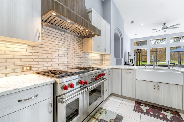 kitchen featuring backsplash, premium range hood, range with two ovens, sink, and light tile patterned floors