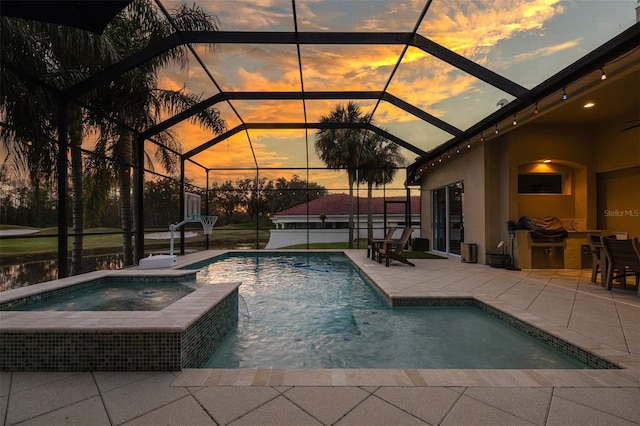 pool at dusk with an in ground hot tub, glass enclosure, and a patio area